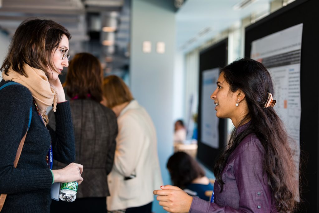 Two women speaking with each other in front of research posters