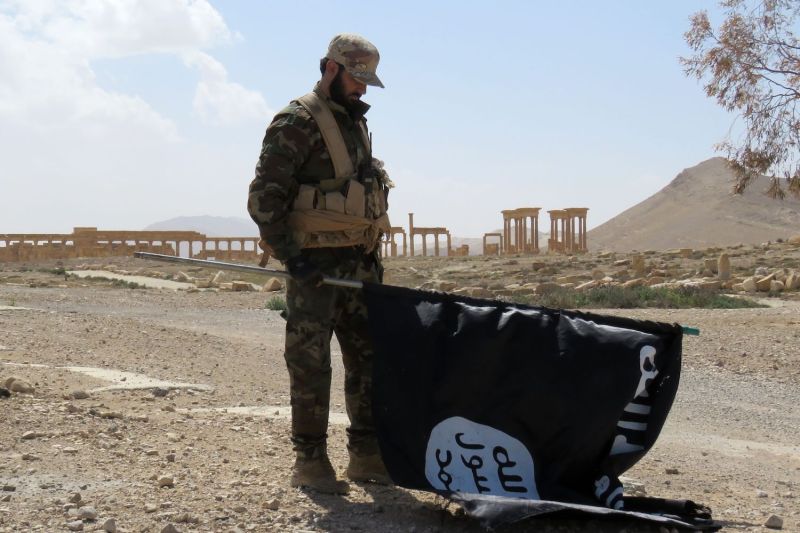 A member of the Syrian pro-government forces carries an Islamic State (IS) group flag as he stands on a street in the ancient city of Palmyra on March 27, 2016, after troops recaptured the city from IS jihadists.