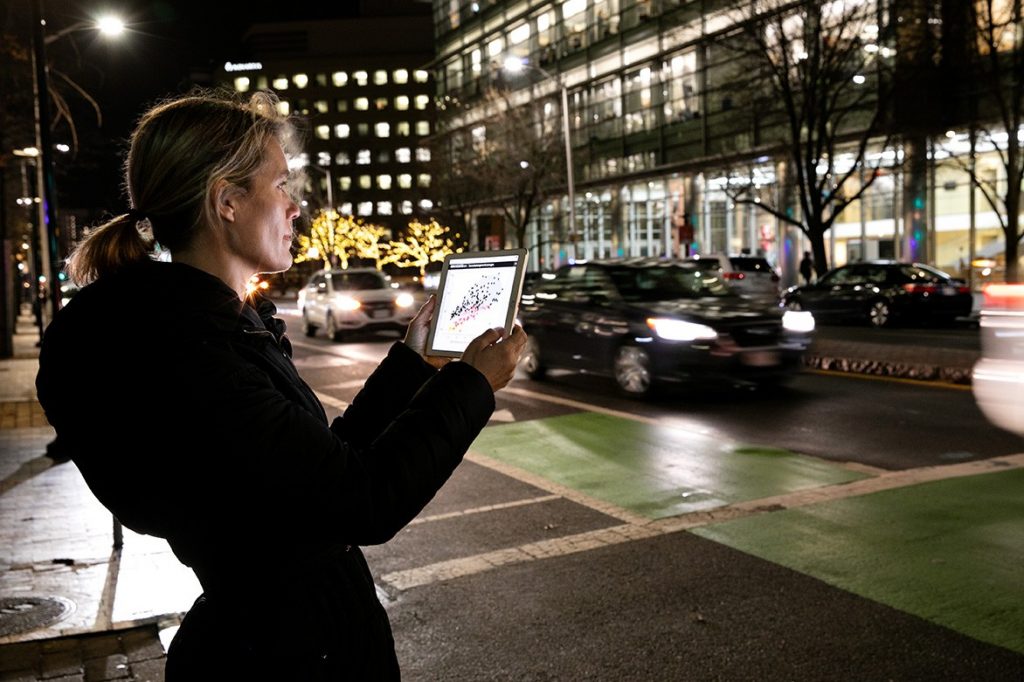 Jessika Trancik looks at data on a tablet while standing next to a busy city street