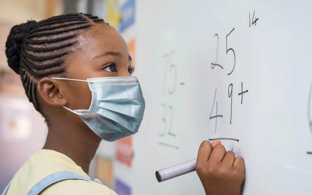 girl wearing a mask writing math equations on a white board