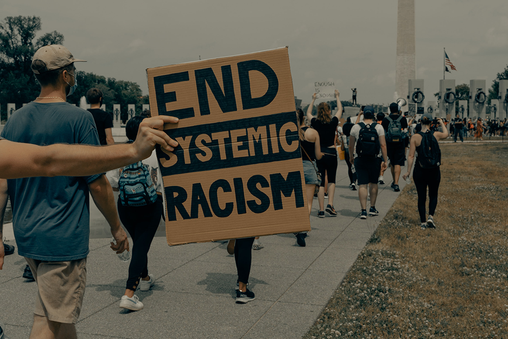 Protest with carboard sign that says End Systemic Racism