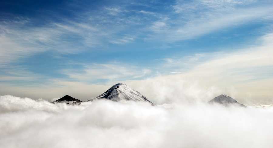 a photo of mountain peaks rising over clouds