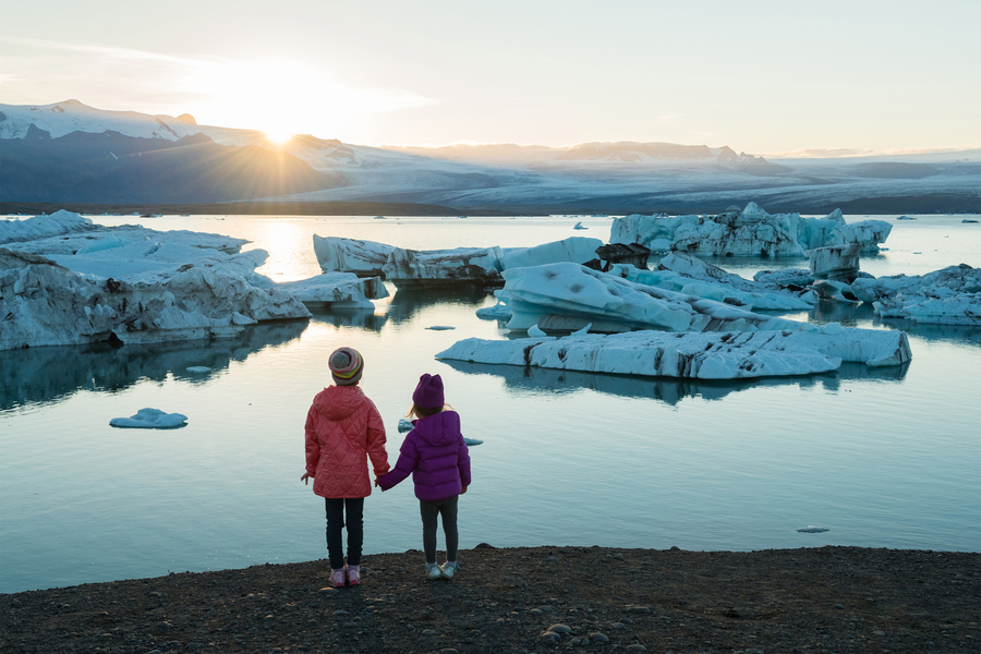two children holding hands and looking at icebergs