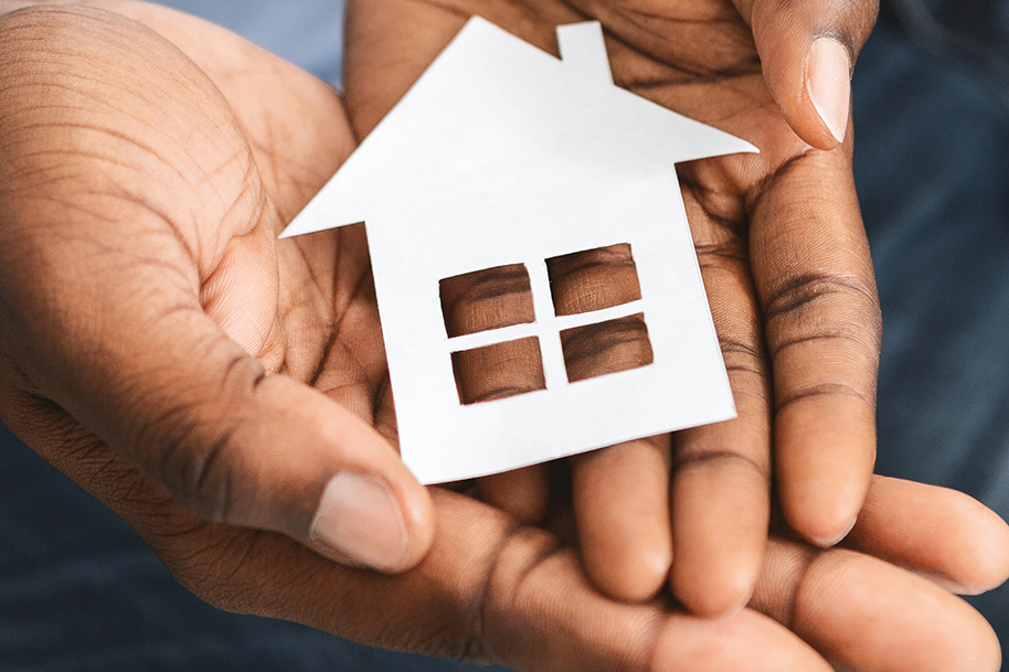 Darker skinned hands holding a paper cutout of a house