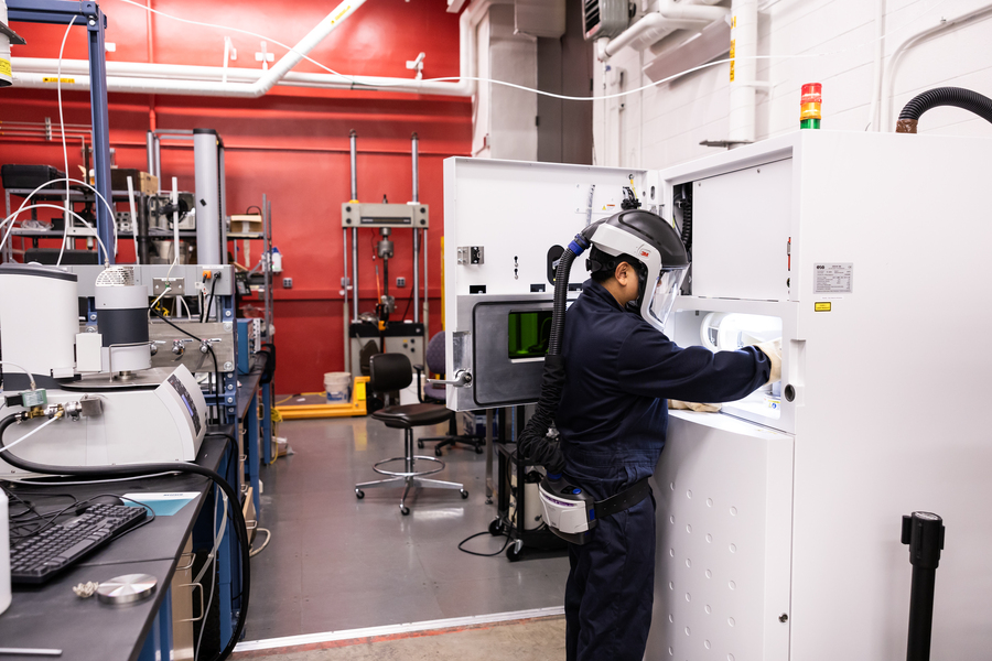 a student in a helmet-style facemask works with unseen manufacturing equipment