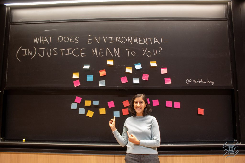 a person stands in front of a blackboard covered in colorful post-it notes under the question 'What does environmental (in)justice mean to you?'