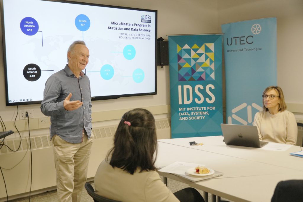 John Tsitsiklis speaks in front of an IDSS banner and screen showing a world map.